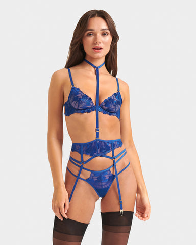 Blue lingerie set including blue sheer bra, harness, suspenders and blue thong worn with black stockings. 